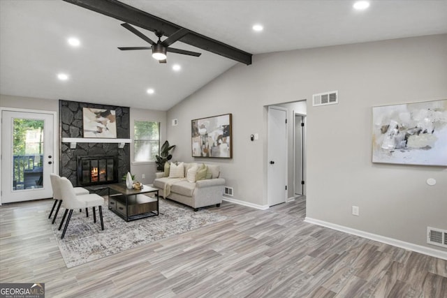 living area featuring vaulted ceiling with beams, visible vents, wood finished floors, and a stone fireplace