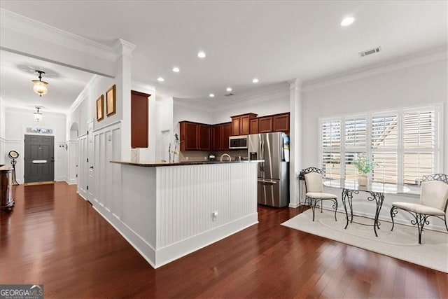 kitchen featuring visible vents, white microwave, dark wood-type flooring, stainless steel fridge, and a peninsula