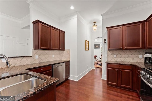 kitchen featuring dark wood finished floors, appliances with stainless steel finishes, ornamental molding, a sink, and dark stone counters