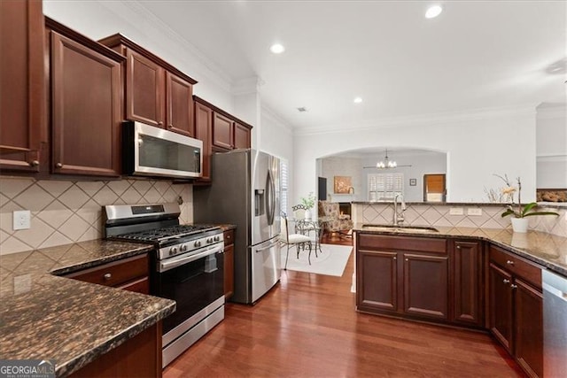 kitchen with arched walkways, a chandelier, stainless steel appliances, dark wood-type flooring, and a sink