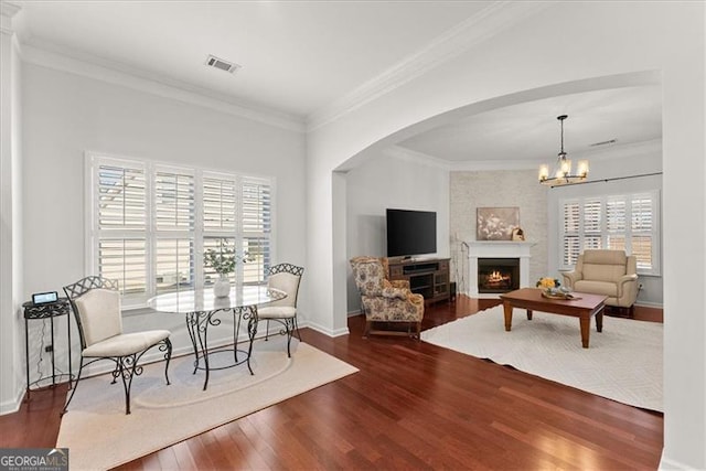 dining room with a warm lit fireplace, ornamental molding, wood finished floors, and a wealth of natural light