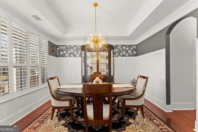 dining room with arched walkways, wood finished floors, a raised ceiling, and a decorative wall