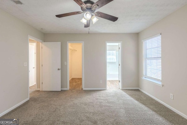 unfurnished bedroom with baseboards, visible vents, a walk in closet, a textured ceiling, and carpet flooring