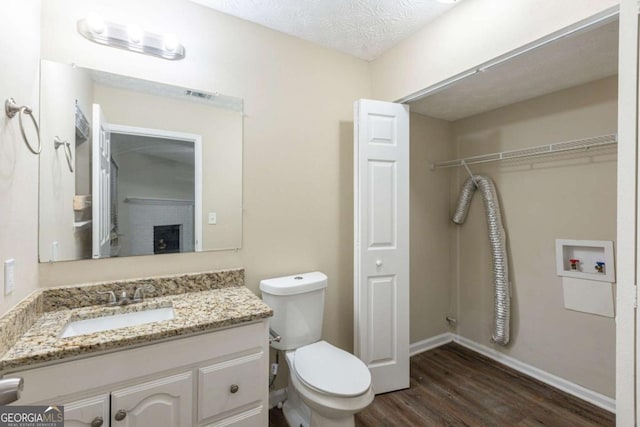 bathroom with a textured ceiling, toilet, wood finished floors, visible vents, and vanity