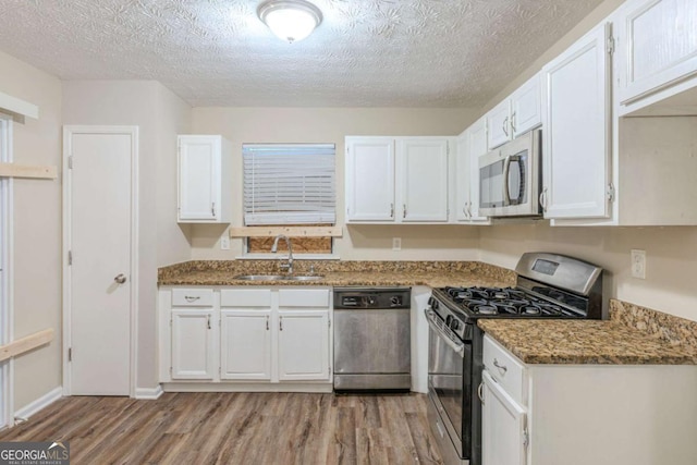 kitchen featuring appliances with stainless steel finishes, white cabinetry, a sink, dark stone countertops, and light wood-type flooring