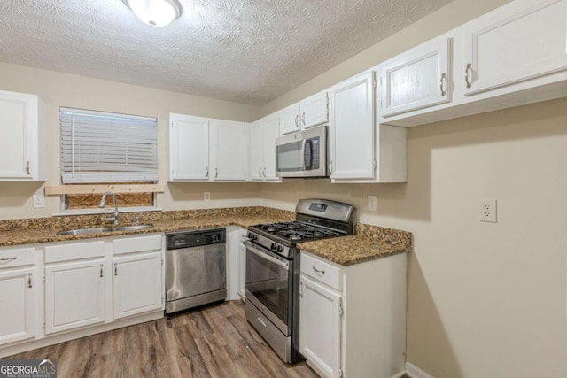 kitchen with dark stone counters, wood finished floors, stainless steel appliances, white cabinetry, and a sink