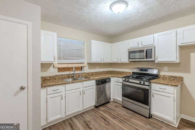 kitchen featuring dark stone countertops, wood finished floors, stainless steel appliances, white cabinetry, and a sink