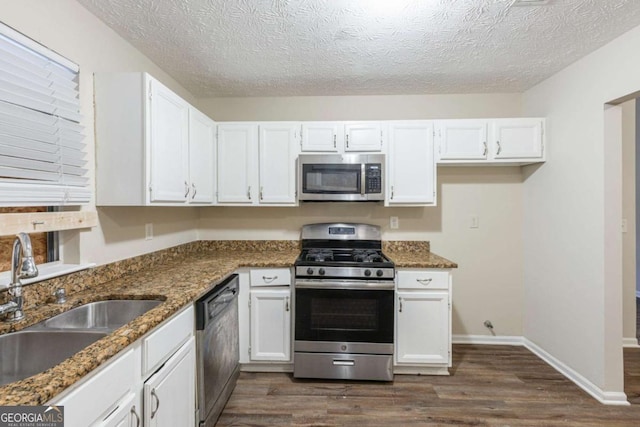 kitchen with appliances with stainless steel finishes, dark wood-style flooring, white cabinets, and a sink