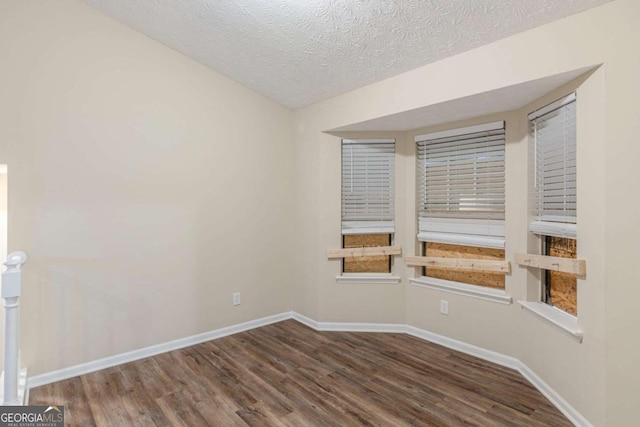 spare room with a textured ceiling, baseboards, and wood finished floors