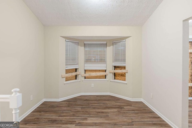 unfurnished room with a textured ceiling, baseboards, and wood finished floors