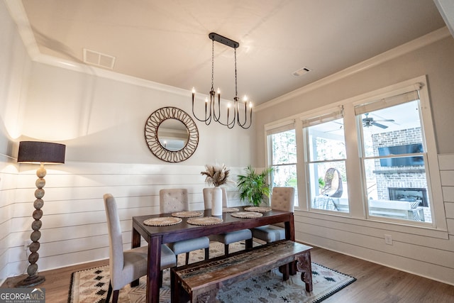 dining room with wooden walls, visible vents, wood finished floors, crown molding, and a notable chandelier