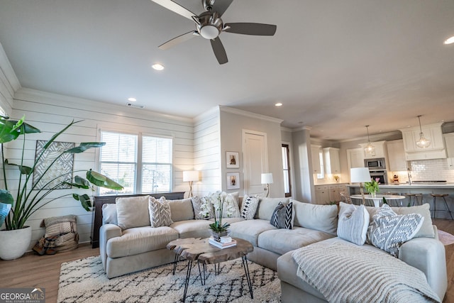 living area with recessed lighting, wood walls, wood finished floors, visible vents, and ornamental molding