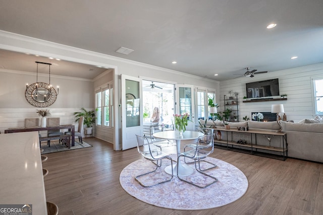 dining space featuring ceiling fan with notable chandelier, a wealth of natural light, a lit fireplace, and wood finished floors