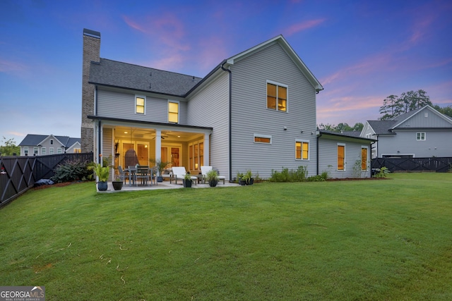 back of house at dusk featuring a yard, a patio, a chimney, ceiling fan, and a fenced backyard