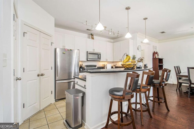 kitchen with dark countertops, visible vents, hanging light fixtures, appliances with stainless steel finishes, and white cabinetry