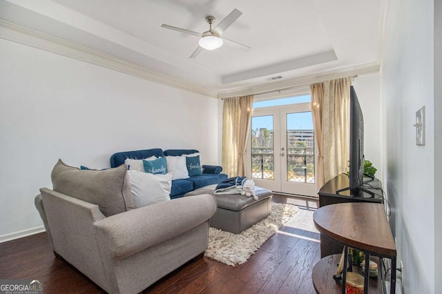 living area featuring a ceiling fan, dark wood-style floors, ornamental molding, a tray ceiling, and french doors