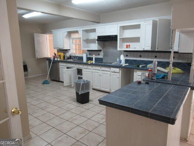 kitchen with light tile patterned floors, under cabinet range hood, white cabinetry, backsplash, and open shelves