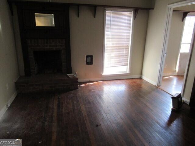 unfurnished living room with a brick fireplace, baseboards, and wood finished floors