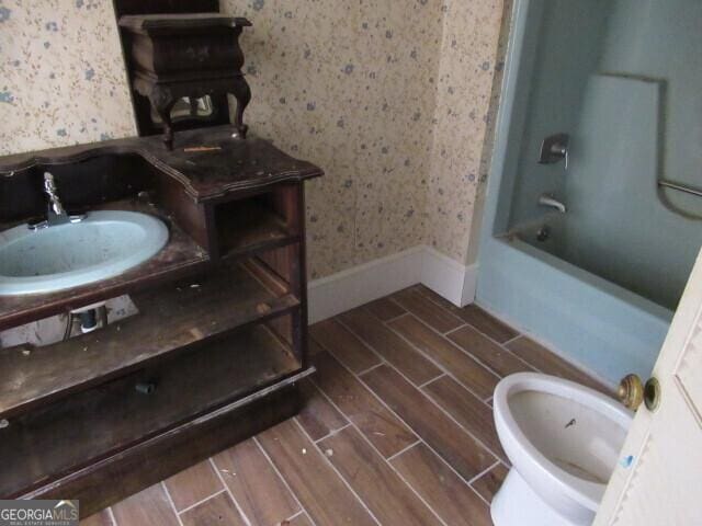 full bathroom featuring wallpapered walls, baseboards, toilet, wood tiled floor, and shower / bathtub combination