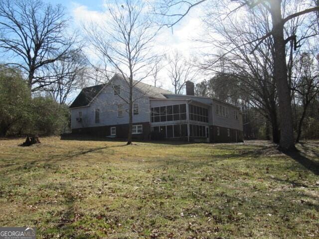 exterior space with a sunroom, a chimney, and a lawn