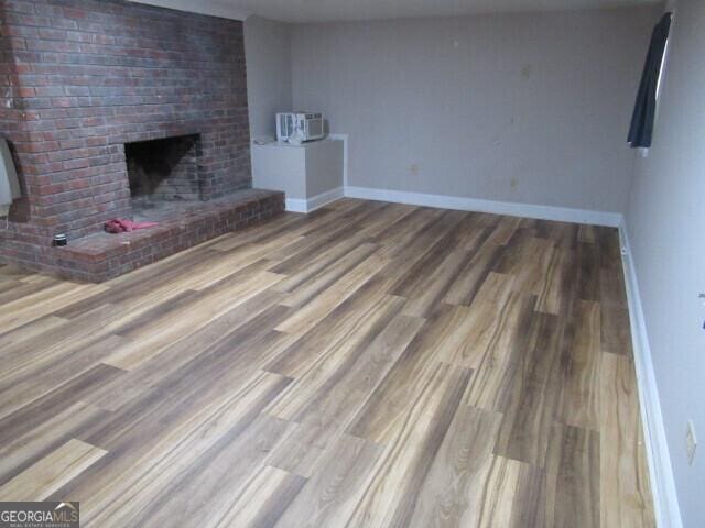 unfurnished living room with an AC wall unit, a fireplace, baseboards, and wood finished floors