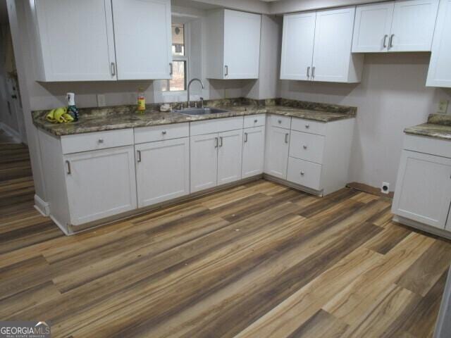 kitchen with dark stone counters, dark wood-style flooring, white cabinets, and a sink