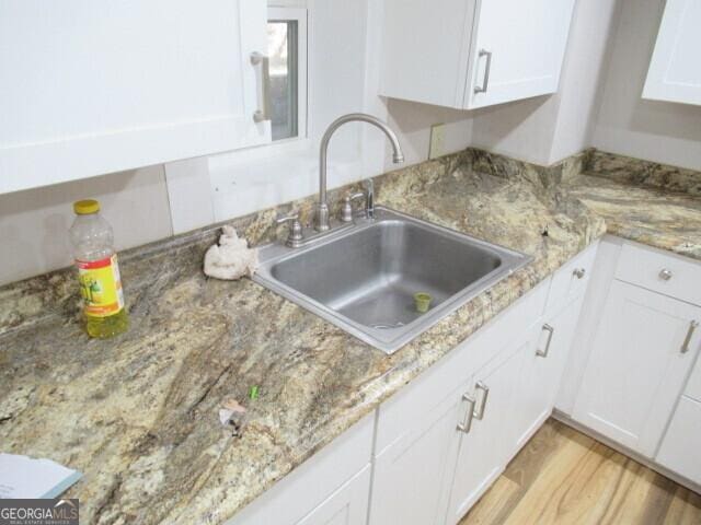 kitchen featuring white cabinetry, a sink, light wood-style flooring, and light stone countertops