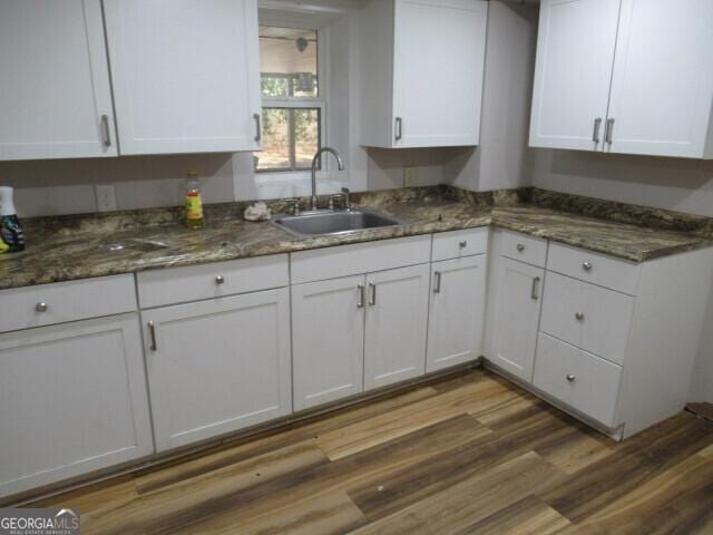 kitchen with white cabinetry, dark stone counters, a sink, and wood finished floors