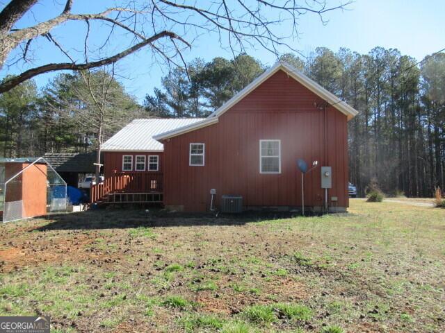 view of side of home featuring metal roof, a lawn, a wooden deck, and central air condition unit