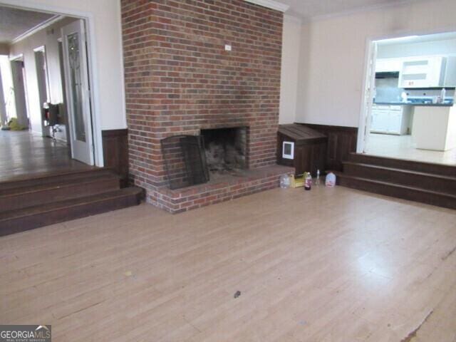 unfurnished living room with ornamental molding, a brick fireplace, and wood finished floors