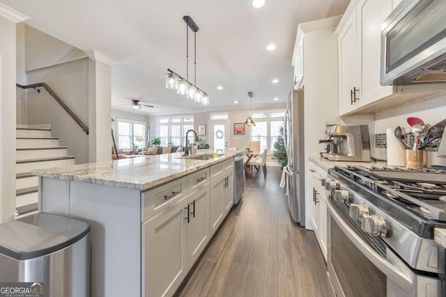 kitchen featuring light stone counters, a center island with sink, stainless steel appliances, white cabinetry, and a sink