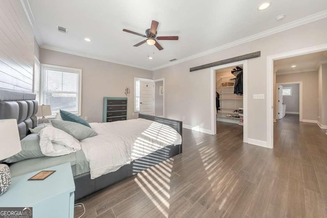 bedroom with a walk in closet, crown molding, visible vents, wood finished floors, and baseboards