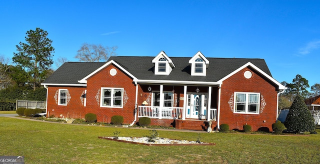 new england style home featuring a front yard, a porch, and brick siding