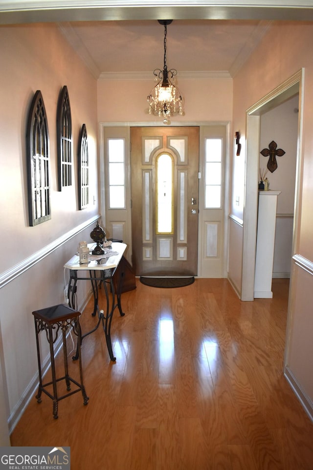 foyer with a notable chandelier, crown molding, and wood finished floors