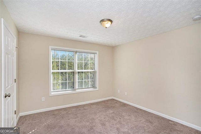 empty room with carpet, visible vents, a textured ceiling, and baseboards