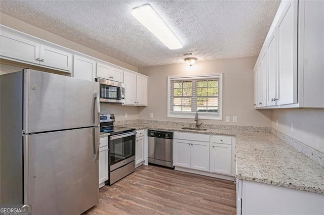 kitchen featuring light stone counters, wood finished floors, stainless steel appliances, white cabinetry, and a sink