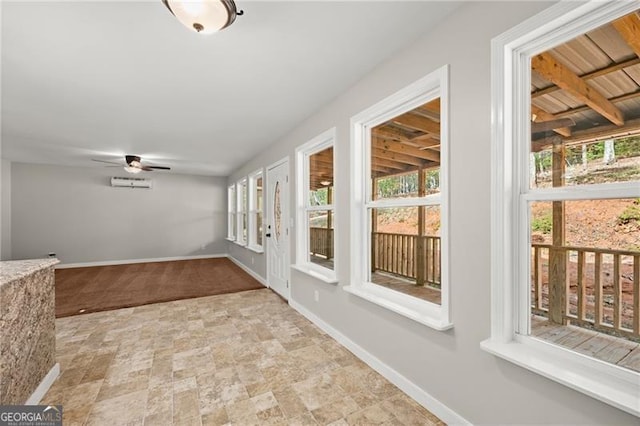 unfurnished sunroom featuring a wall mounted AC, a ceiling fan, and a healthy amount of sunlight