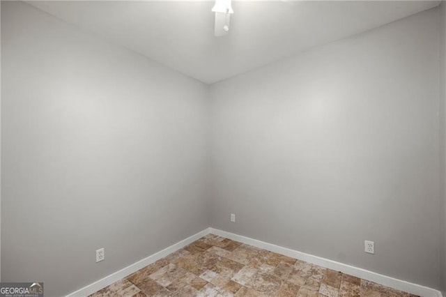 spare room with a ceiling fan, stone finish floor, and baseboards