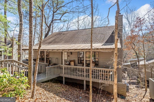 rear view of house with a shingled roof, a chimney, and a deck