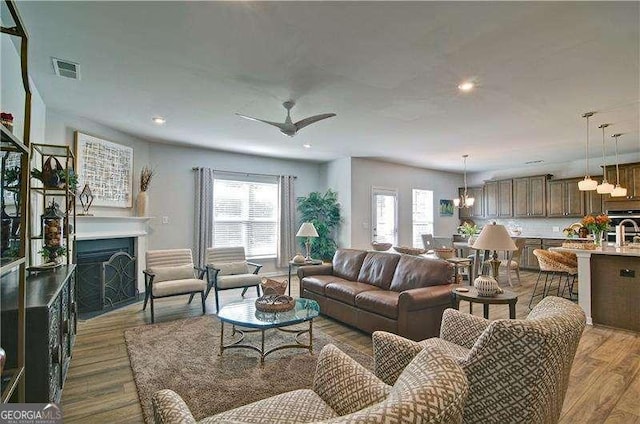 living room with recessed lighting, ceiling fan with notable chandelier, a fireplace, wood finished floors, and visible vents