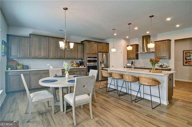 kitchen with a spacious island, wall chimney exhaust hood, stainless steel appliances, and light wood-style flooring