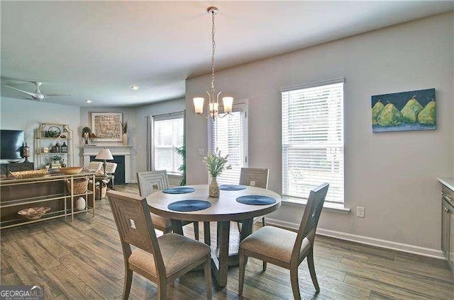 dining area featuring dark wood-style flooring, a fireplace, recessed lighting, baseboards, and ceiling fan with notable chandelier