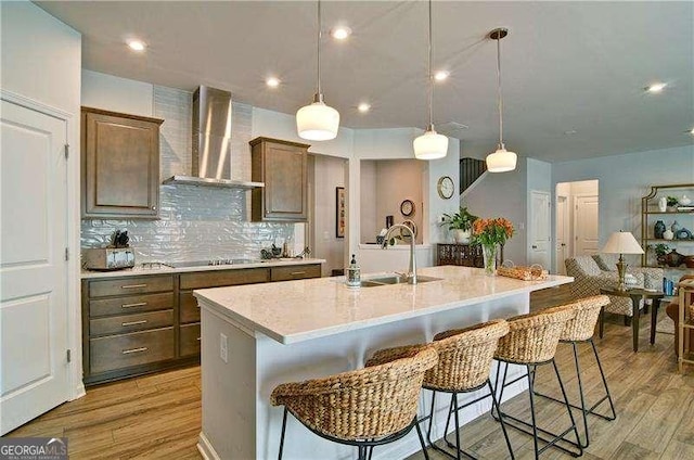 kitchen with light wood-style floors, light countertops, a sink, and wall chimney range hood