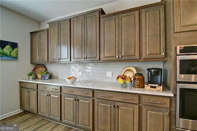 kitchen featuring light countertops, tasteful backsplash, stainless steel double oven, and wood finished floors