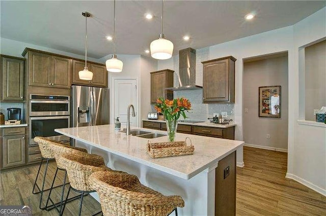 kitchen featuring stainless steel appliances, a sink, light countertops, wall chimney exhaust hood, and tasteful backsplash