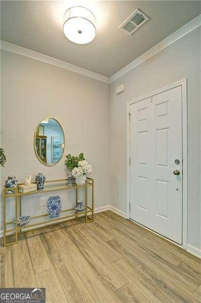 foyer entrance featuring baseboards, crown molding, visible vents, and wood finished floors