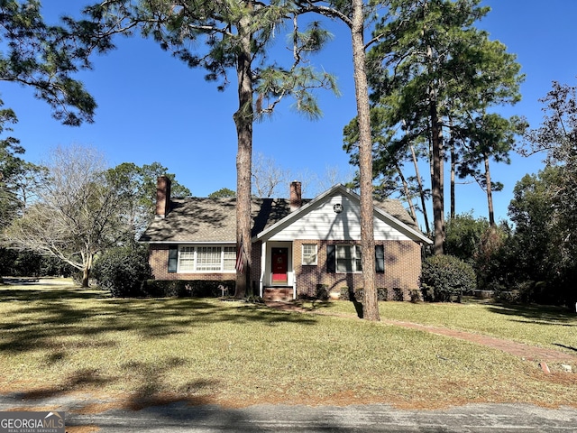 view of front of house featuring entry steps, a front yard, a chimney, and brick siding