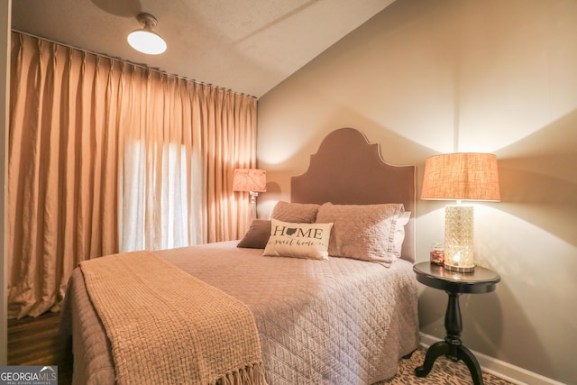 bedroom featuring lofted ceiling, baseboards, and wood finished floors