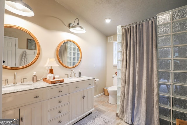 bathroom with a textured ceiling, double vanity, a sink, and toilet