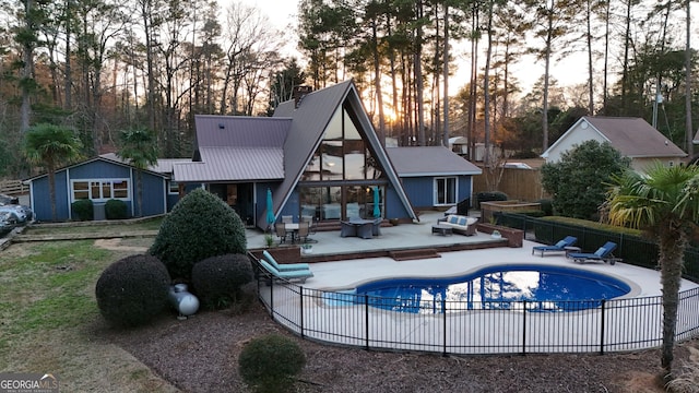 back of property with metal roof, a patio area, fence, and a fenced in pool